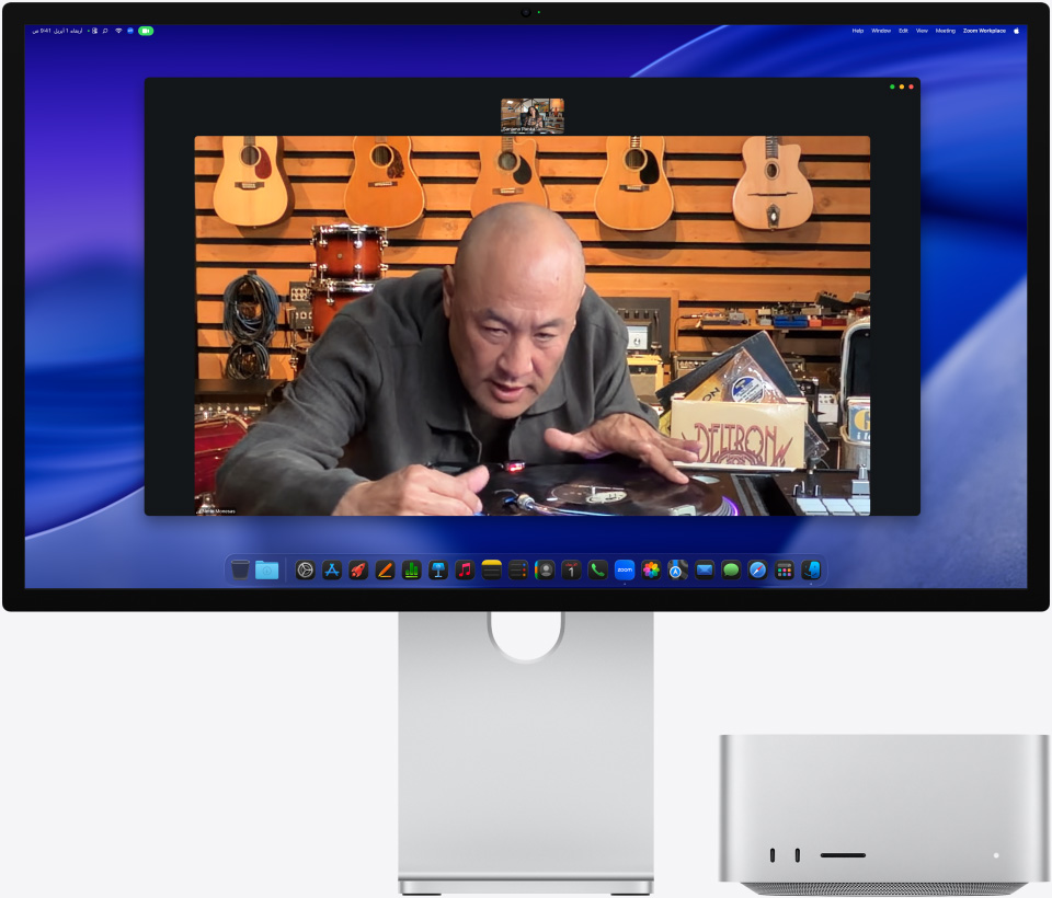 أثناء إجراء مكالمة فيديو على شاشة Studio Display XDR مع جهاز Mac Studio موضوعة تحتها، شخص في متجر موسيقى ينظر عن كثب إلى مشغّل أسطوانات، بينما يبقيه نمط 'في الوسط' في وسط الإطار