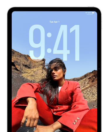 Un iPad affiche l’écran verrouillé où les chiffres de l’heure apparaissent derrière la photo d’une personne assise